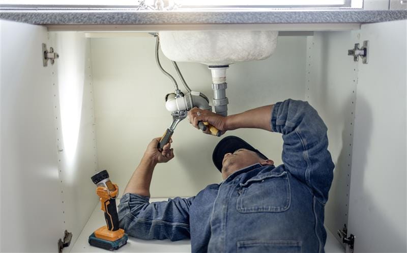 Plumber repairing pipes beneath a bathroom sink in Carson